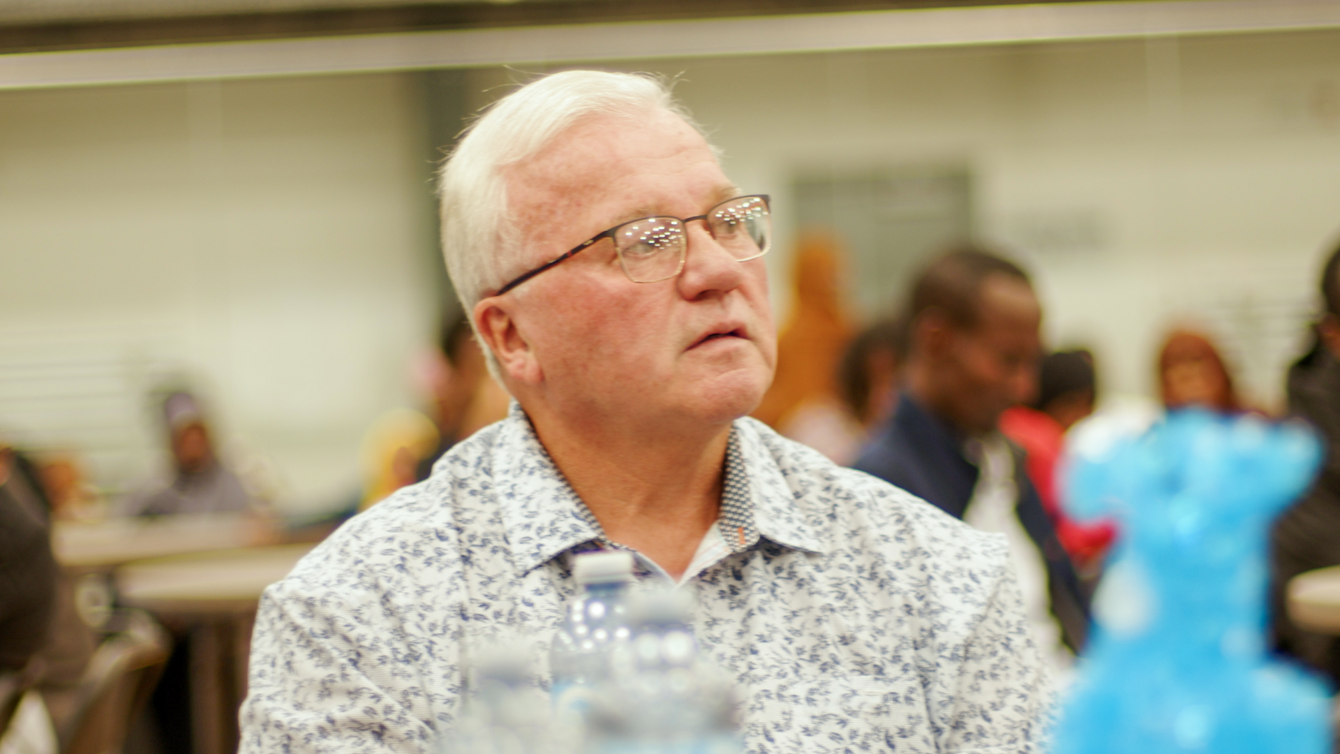 Mayor John Petrie sits attentively at a table, listening to the speaker at the event.